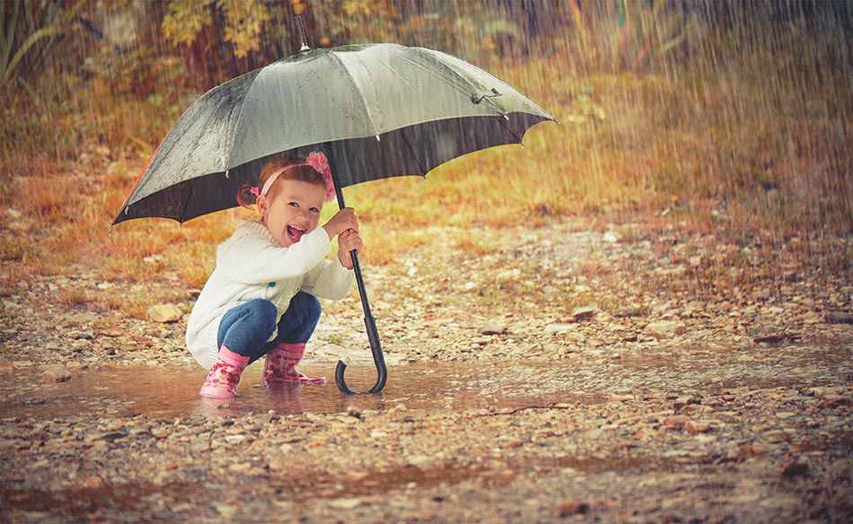 Kind in Pfütze mit grünen Regenschirm in der Hand