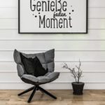 Genieße jeden Moment - Sessel vor Holzwand mit Spruch